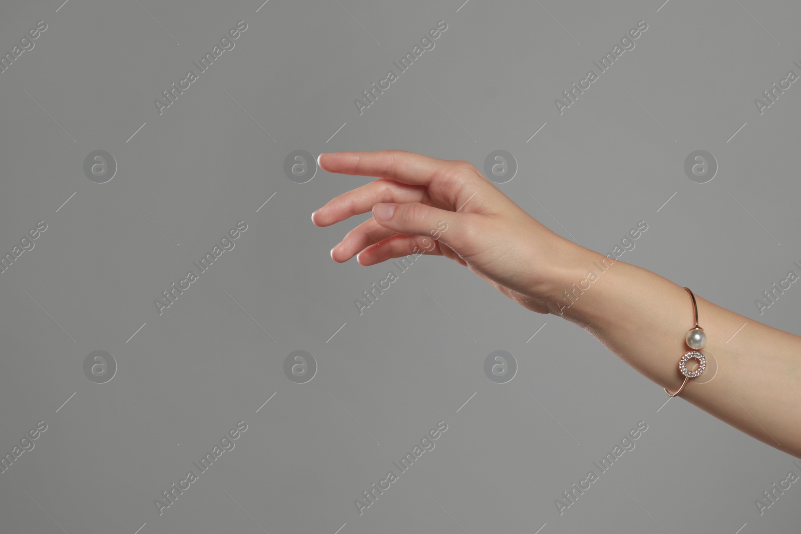 Photo of Young woman wearing elegant bracelet with pearl on grey background, closeup. Space for text