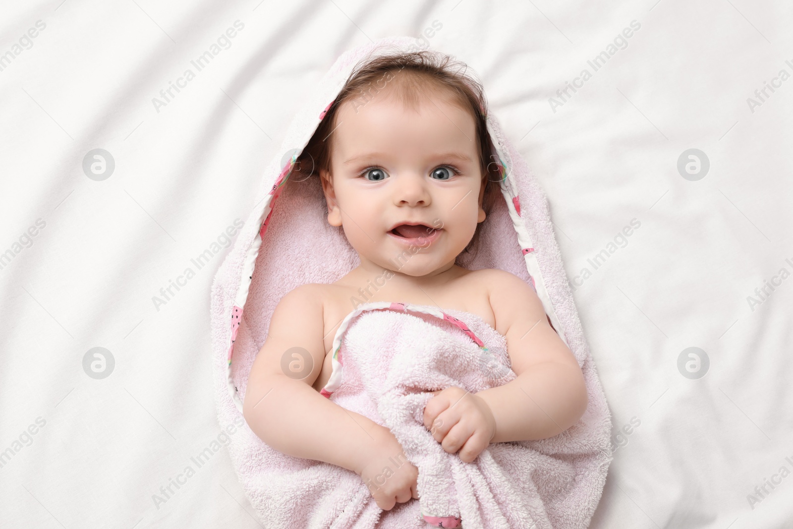 Photo of Cute little baby in hooded towel after bathing on bed, top view