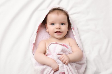 Cute little baby in hooded towel after bathing on bed, top view