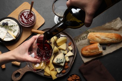Photo of Man pouring red wine from bottle into glass over black table with snacks, top view