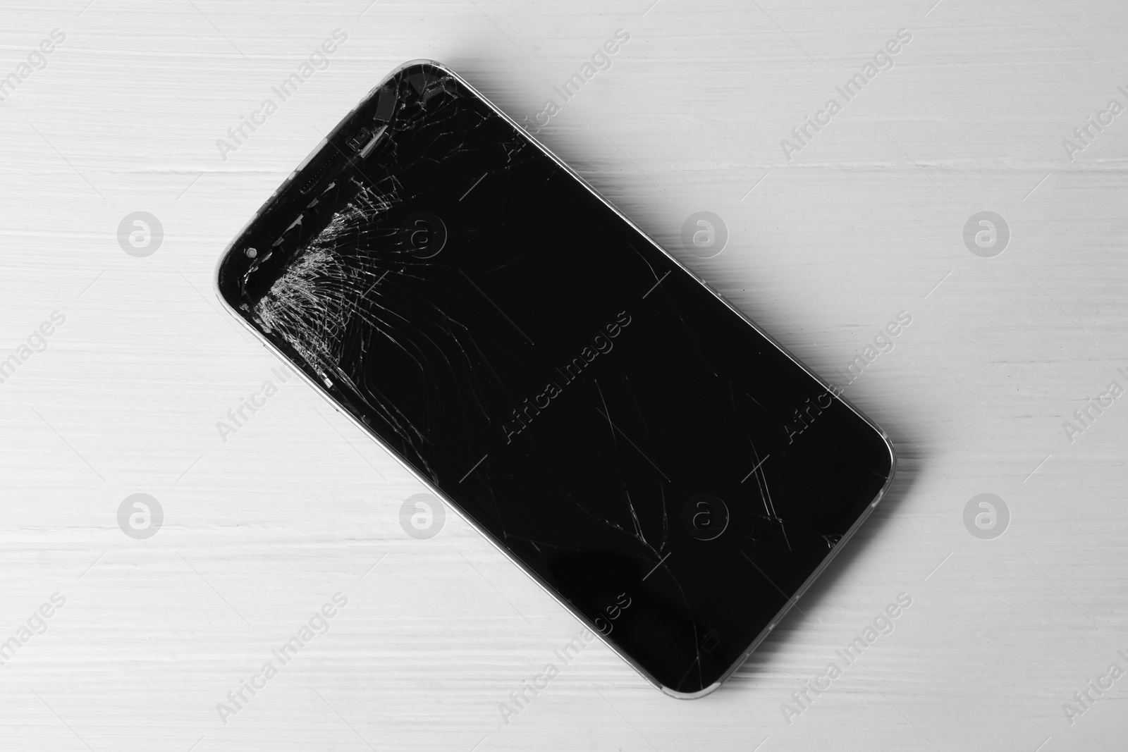 Photo of Damaged smartphone on white wooden table, top view. Device repairing