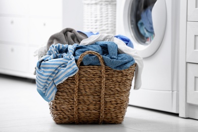 Photo of Wicker basket with dirty laundry on floor indoors