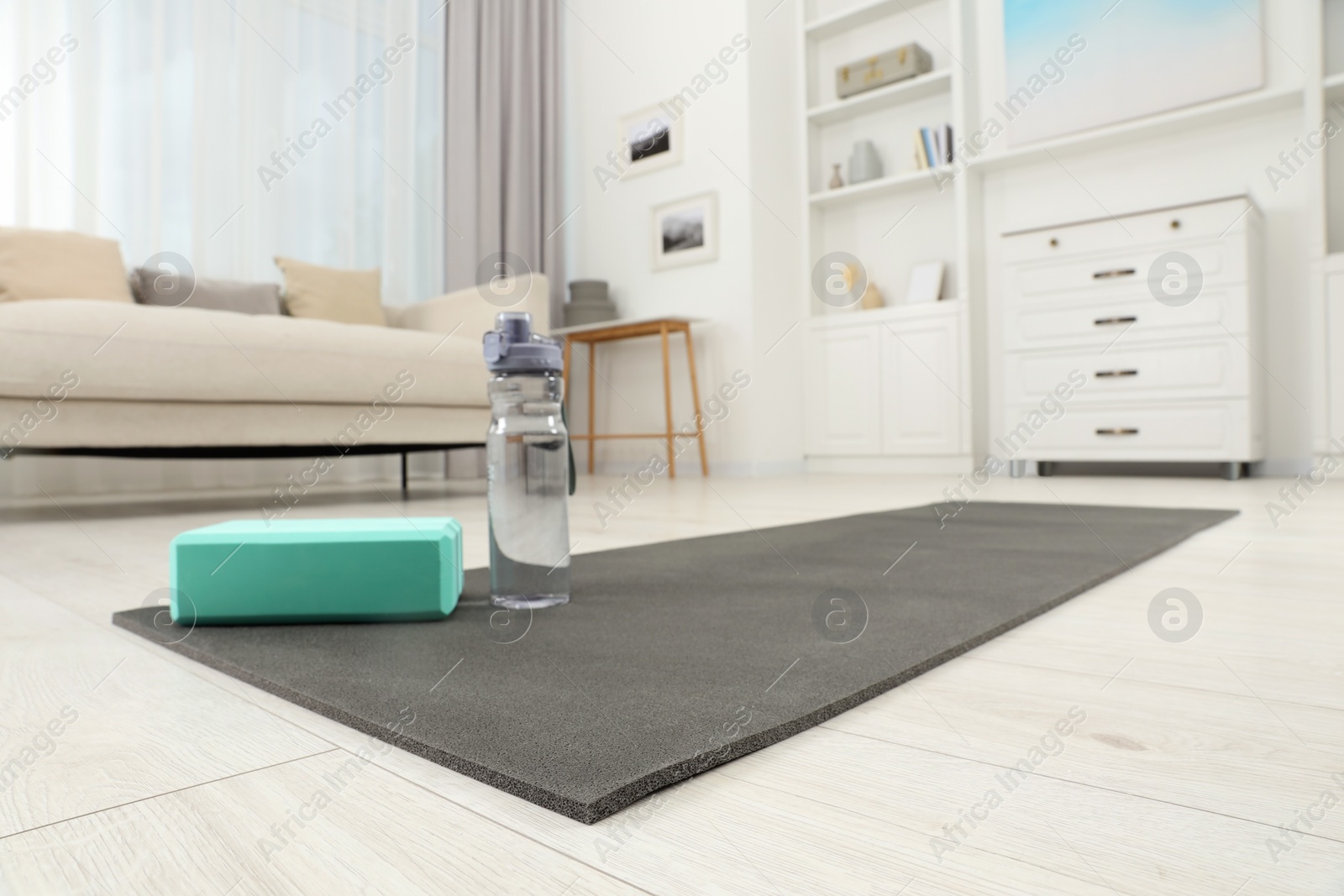 Photo of Exercise mat, yoga block and bottle of water on floor in room