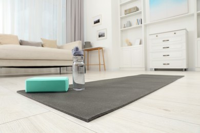Exercise mat, yoga block and bottle of water on floor in room