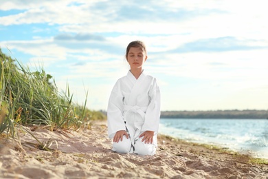 Cute little girl in kimono meditating near river. Karate practicing