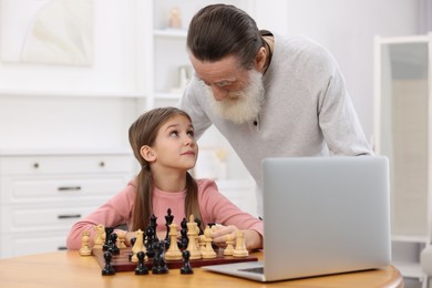 Photo of Grandfather teaching his granddaughter to play chess following online lesson at home