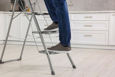 Photo of Man climbing up metal stepladder indoors, closeup