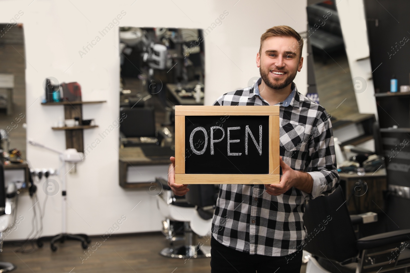 Photo of Young business owner holding OPEN sign in his barber shop