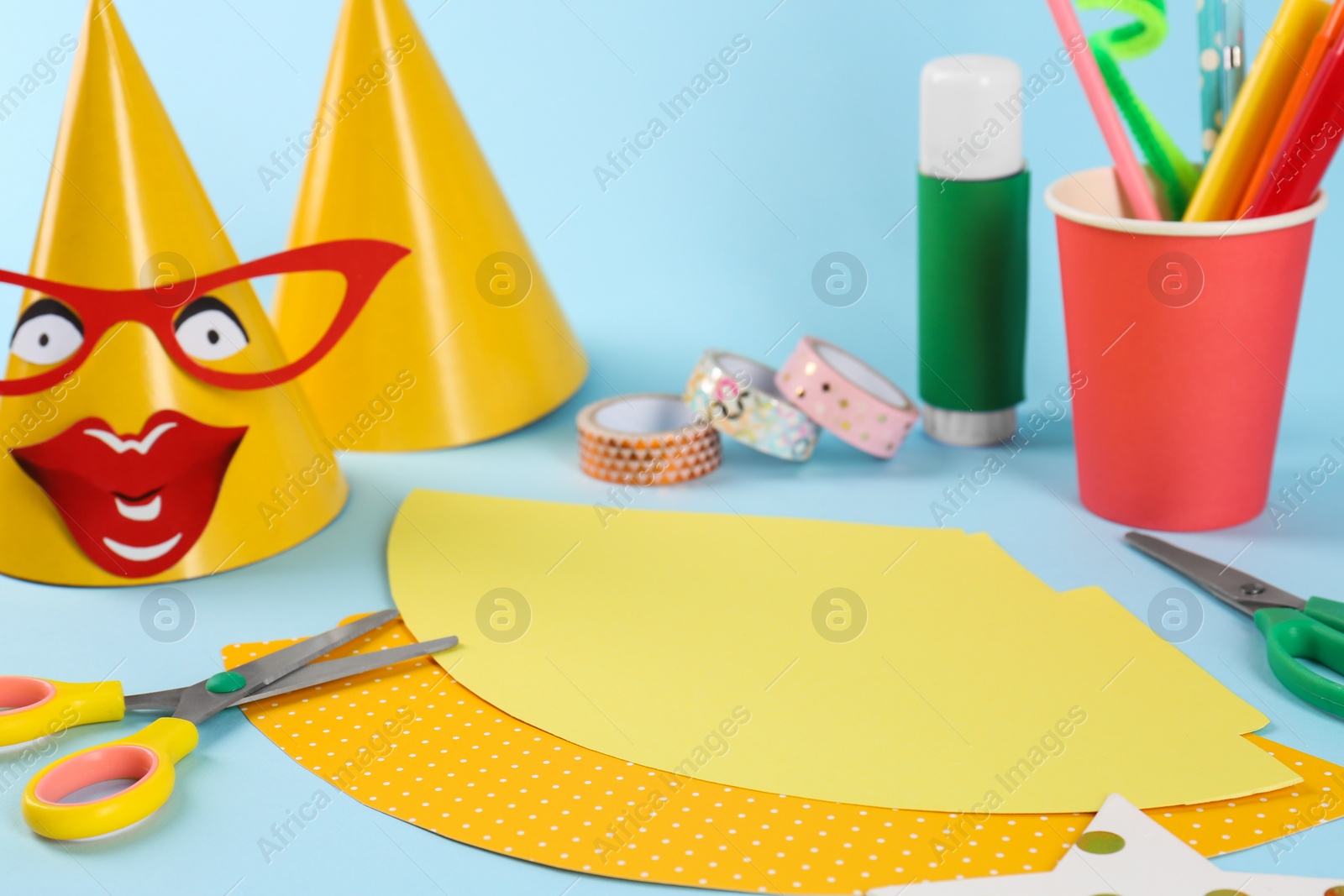 Photo of Different materials and stationery to create party hats on light blue background. Handmade decoration