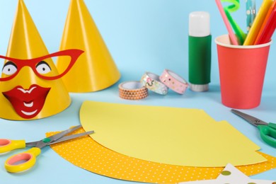 Photo of Different materials and stationery to create party hats on light blue background. Handmade decoration