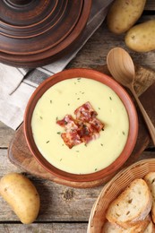 Photo of Tasty potato soup with bacon and rosemary in bowl served on wooden table, flat lay