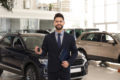 Salesman with key and clipboard in car salon