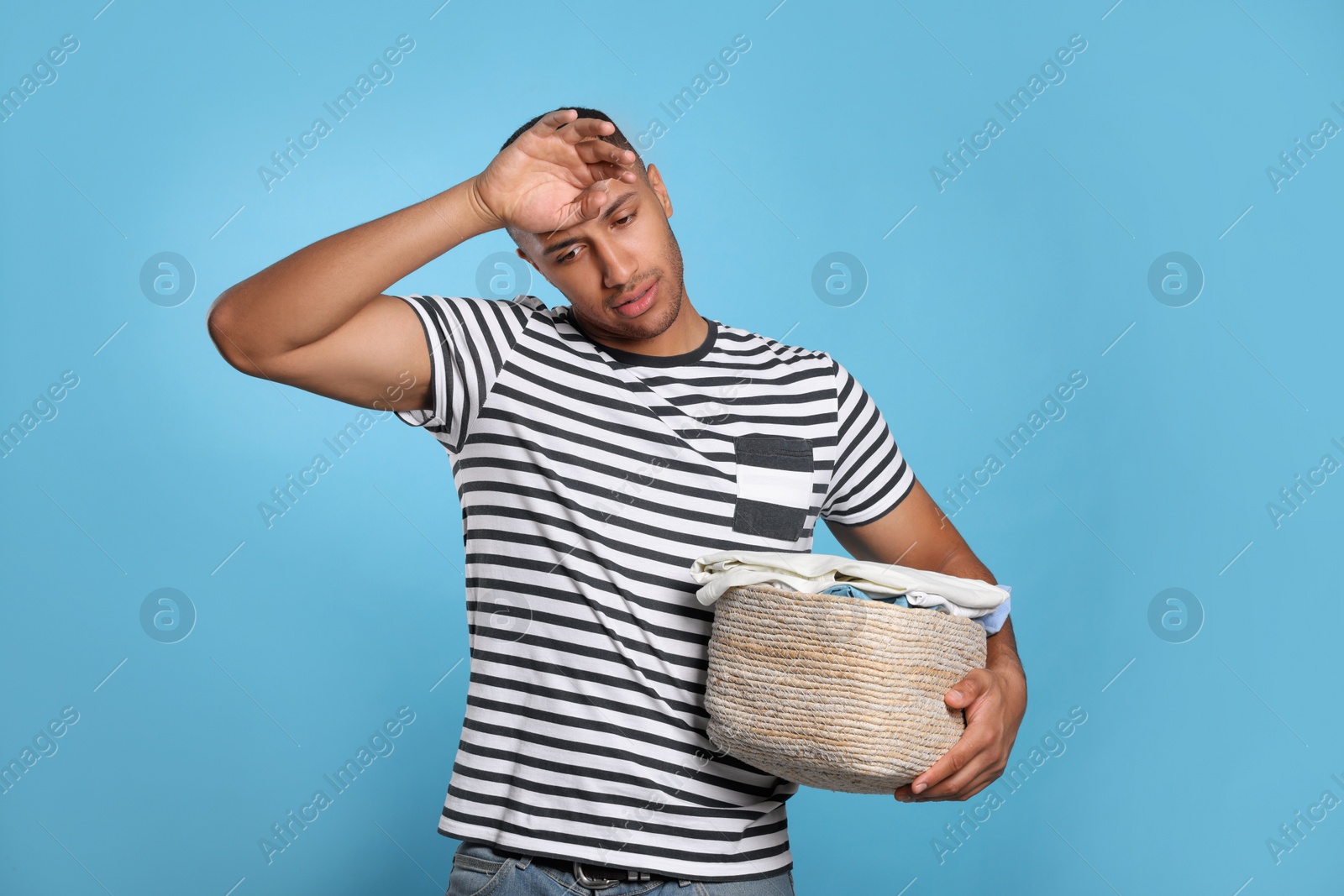 Photo of Tired man with basket full of laundry on light blue background