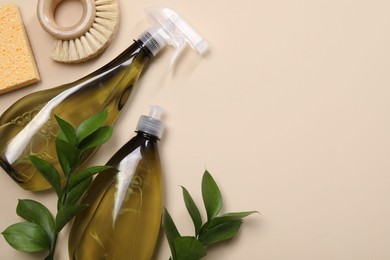 Photo of Bottles of cleaning product, brush, sponge and floral decor on beige background, flat lay. Space for text