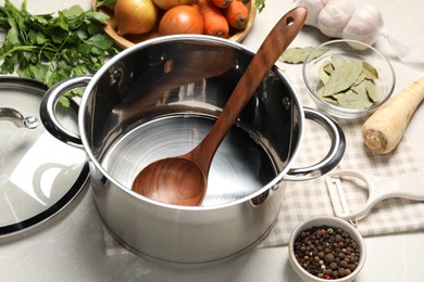 Photo of Pot with ladle and different ingredients for cooking tasty bouillon on light table
