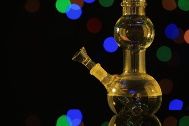 Photo of Closeup view of glass bong against blurred lights, toned in yellow. Smoking device