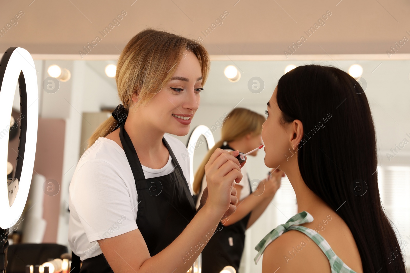Photo of Professional makeup artist working with beautiful young woman in salon. Using ring lamp