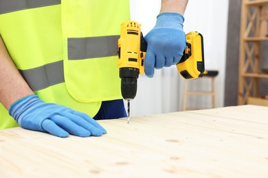 Young worker using electric drill at table in workshop, closeup