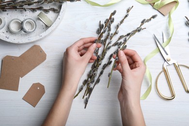 Photo of Woman making beautiful bouquet of pussy willow branches at white wooden table, top view