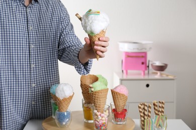 Photo of Woman holding waffle cone with cotton candy indoors, closeup