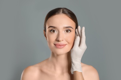 Photo of Doctor examining woman's face before plastic surgery on grey background