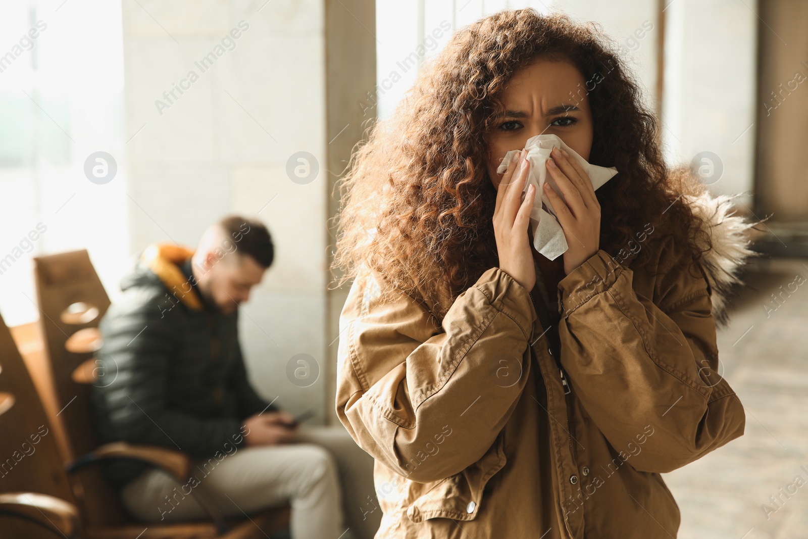 Photo of Young African-American woman sneezing indoors. Influenza virus