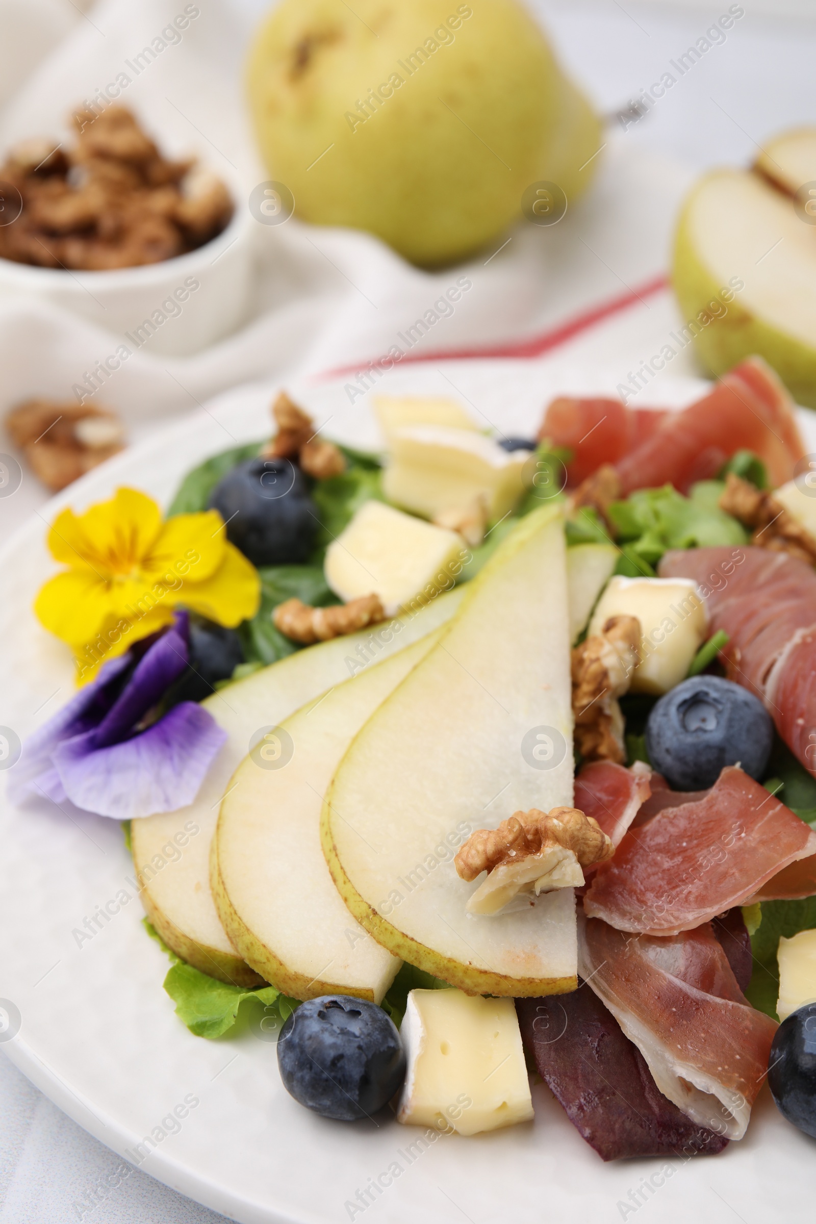 Photo of Tasty salad with brie cheese, prosciutto, walnuts and pear on white plate, closeup