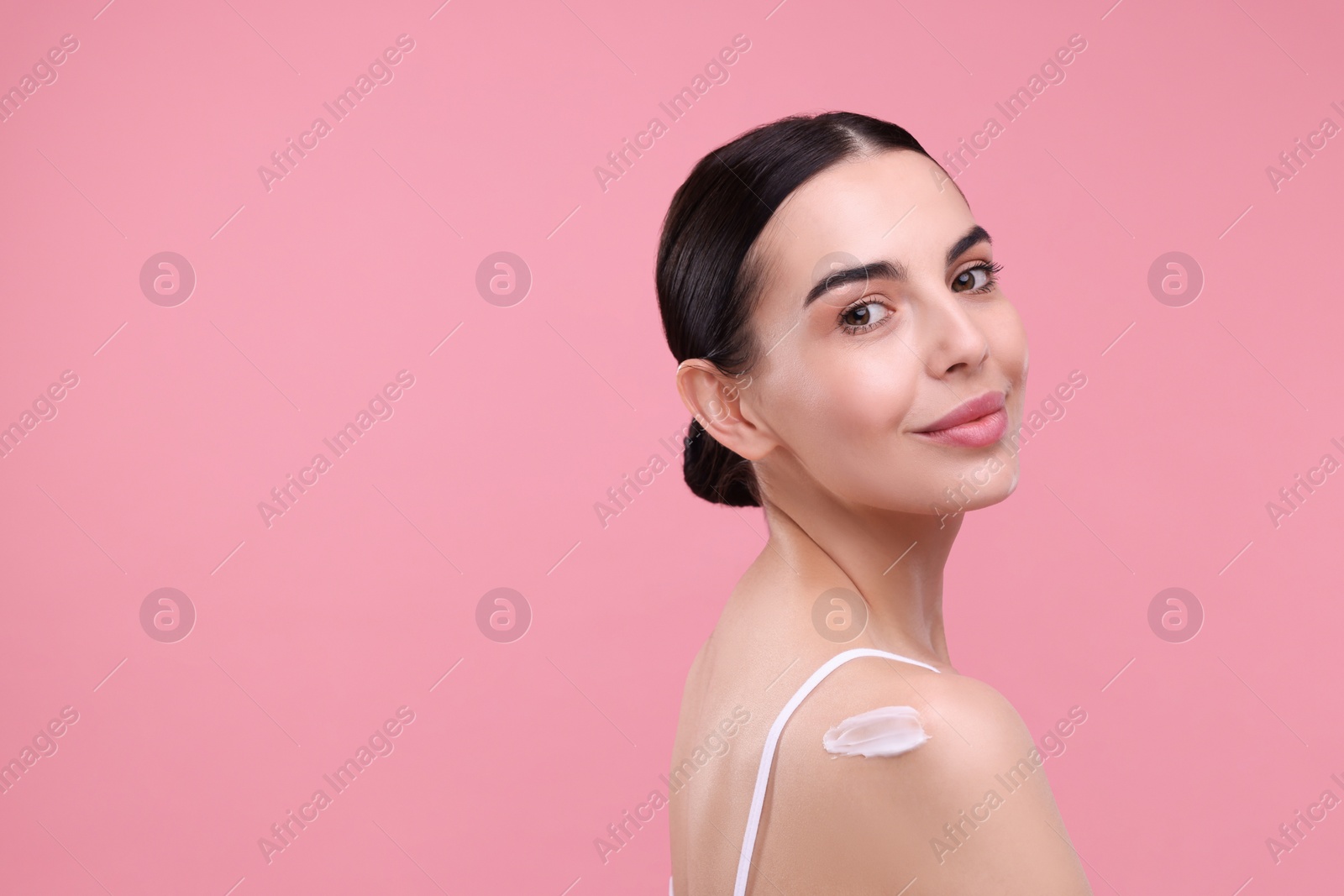 Photo of Beautiful woman with smear of body cream on her shoulder against pink background, space for text
