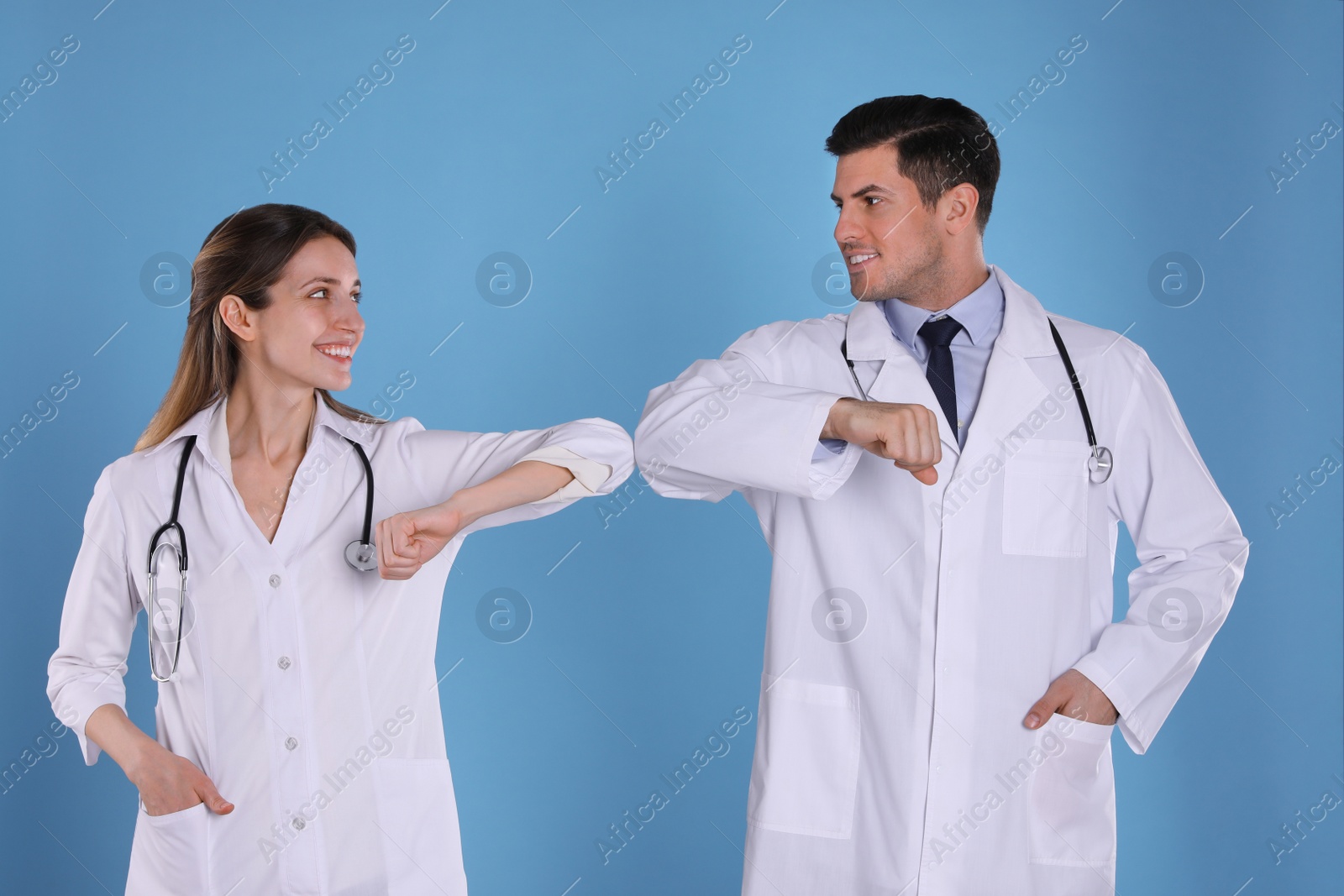 Photo of Doctors greeting each other by bumping elbows instead of handshake on light blue background