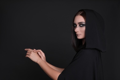 Photo of Mysterious witch in mantle with hood on black background