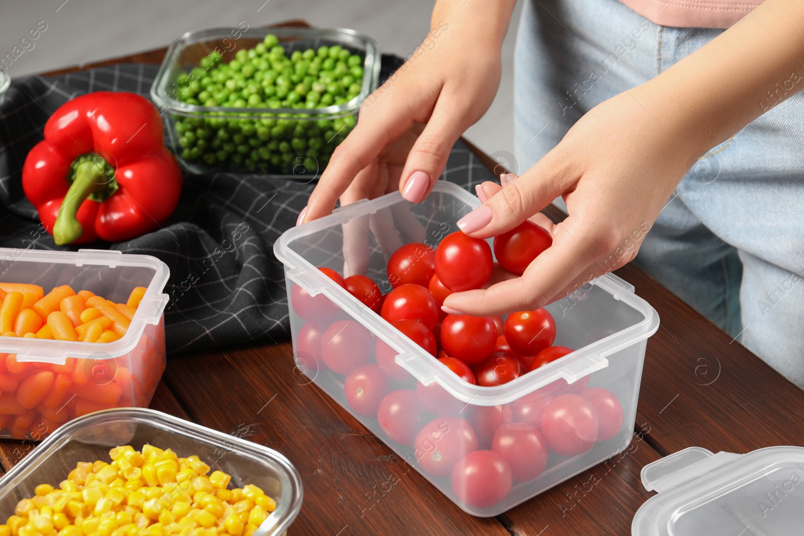 Photo of Woman putting tomatoes into plastic container at wooden table, closeup. Food storage