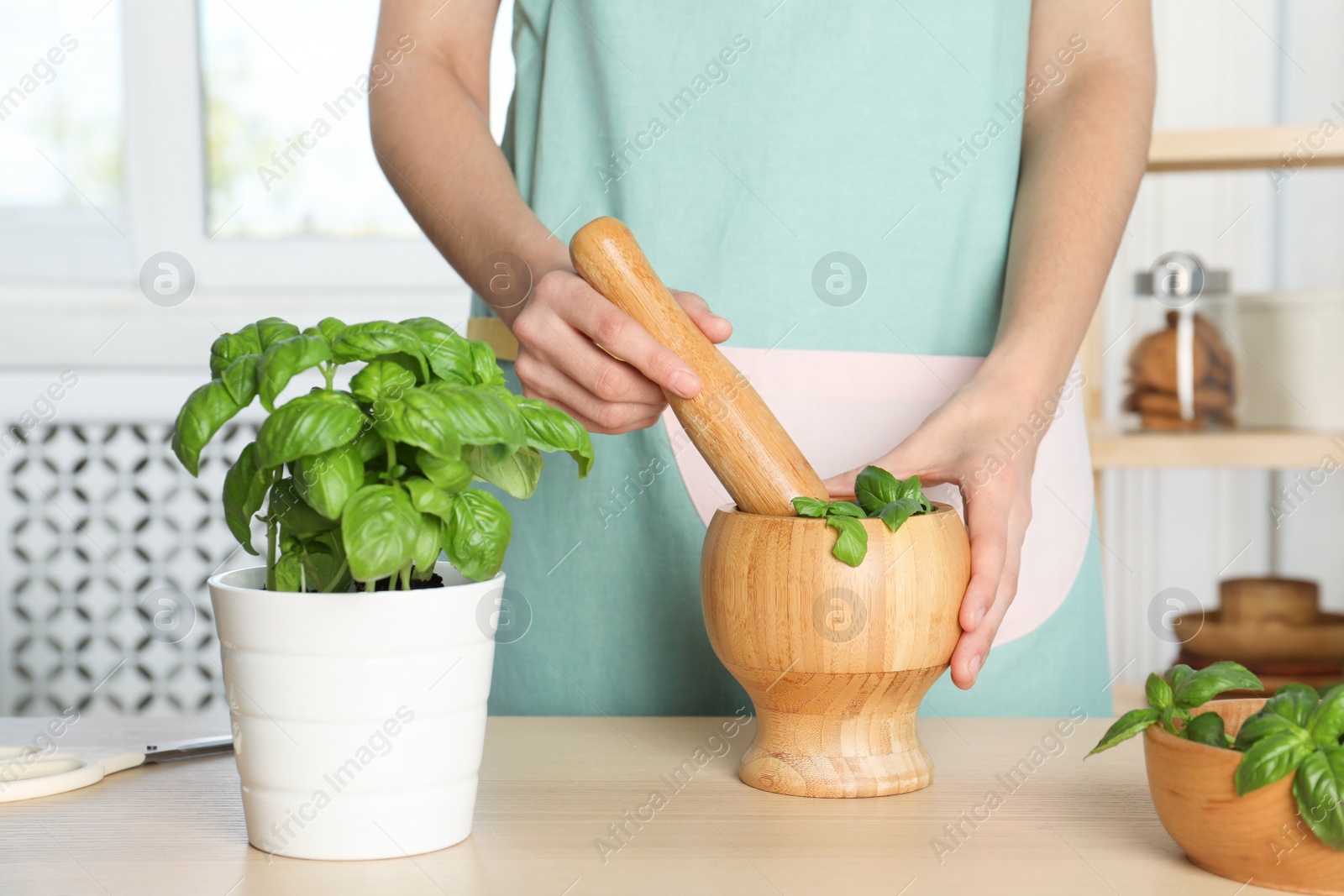 Photo of Woman grinding green basil in mortar at kitchen table