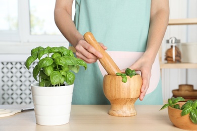 Woman grinding green basil in mortar at kitchen table