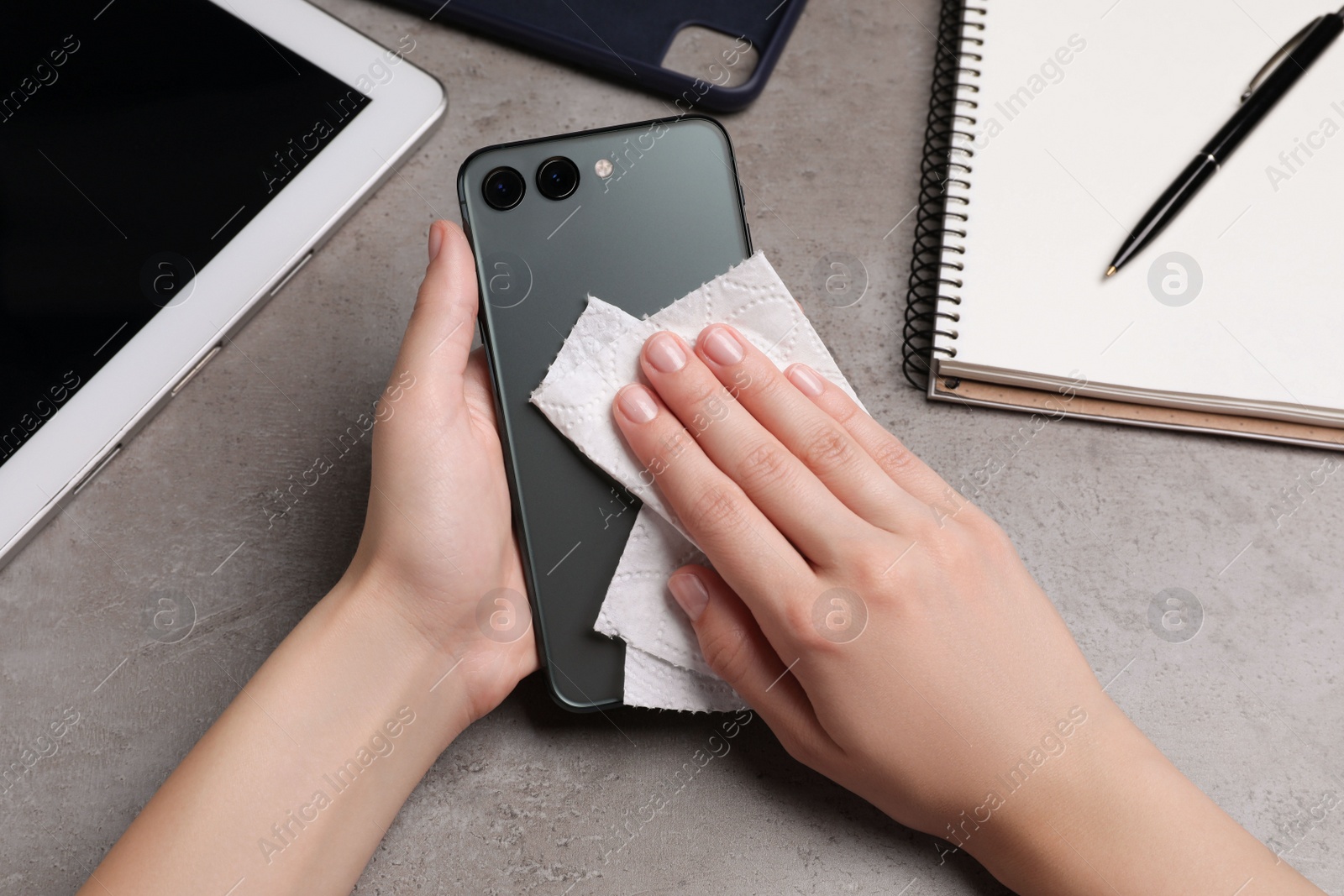 Photo of Woman wiping smartphone with paper towel at gray table, closeup