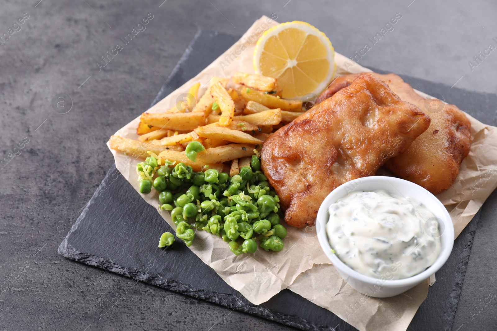 Photo of Tasty fish, chips, sauce and peas on grey table, closeup