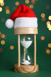 Photo of Hourglass and Santa hat on green background. Christmas countdown