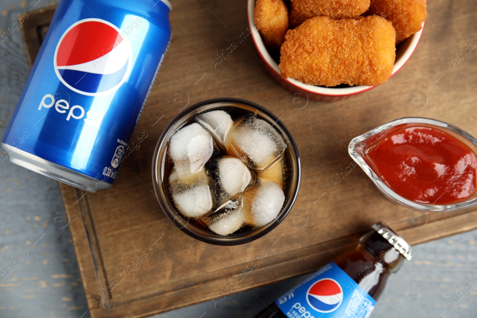 Photo of MYKOLAIV, UKRAINE - FEBRUARY 15, 2021: Different Pepsi drinks and snack on grey wooden table, flat lay