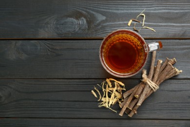 Photo of Aromatic licorice tea in cup and dried sticks of licorice root on black wooden table, flat lay. Space for text