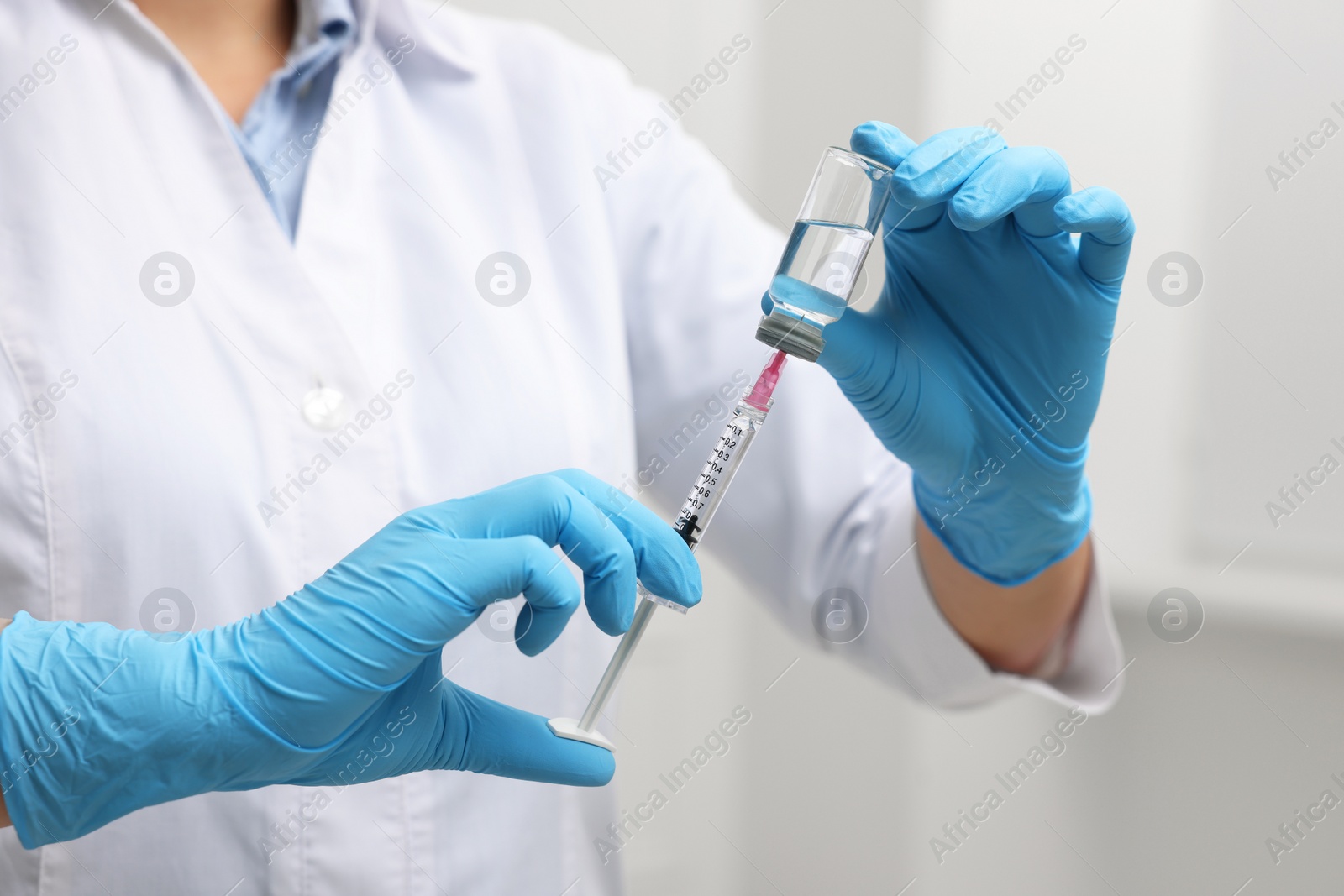 Photo of Doctor filling syringe with medication from glass vial indoors, closeup