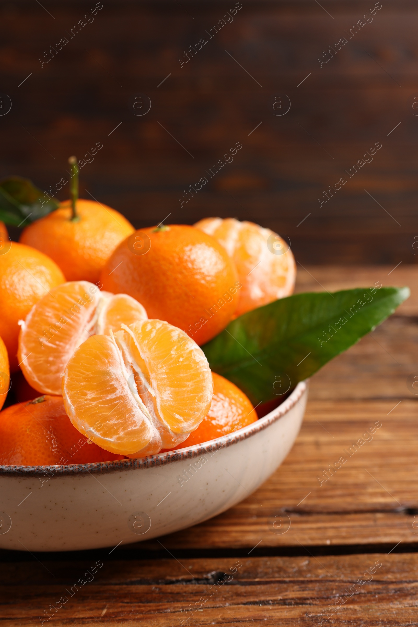 Photo of Fresh tangerines with green leaves in bowl on wooden table, closeup