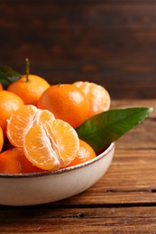 Fresh tangerines with green leaves in bowl on wooden table, closeup