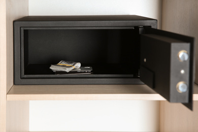 Photo of Open steel safe with money and smartphone in wooden closet