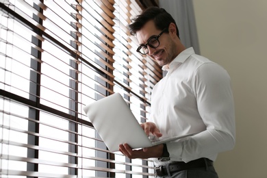 Handsome young man with laptop near window indoors