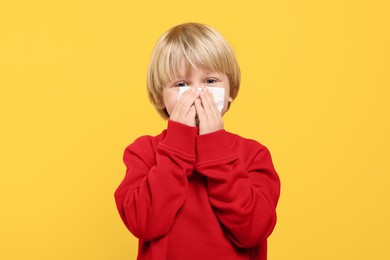 Photo of Boy blowing nose in tissue on orange background. Cold symptoms