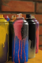 Photo of Used cans of spray paints on table near brick wall, closeup. Graffiti supplies