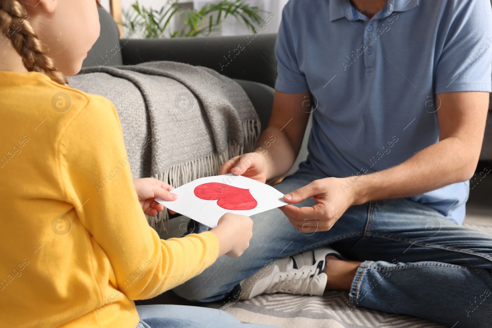 Photo of Man receiving greeting card from his little daughter at home, closeup