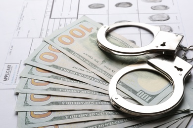 Money, handcuffs and fingerprint record sheets, closeup. Criminal investigation