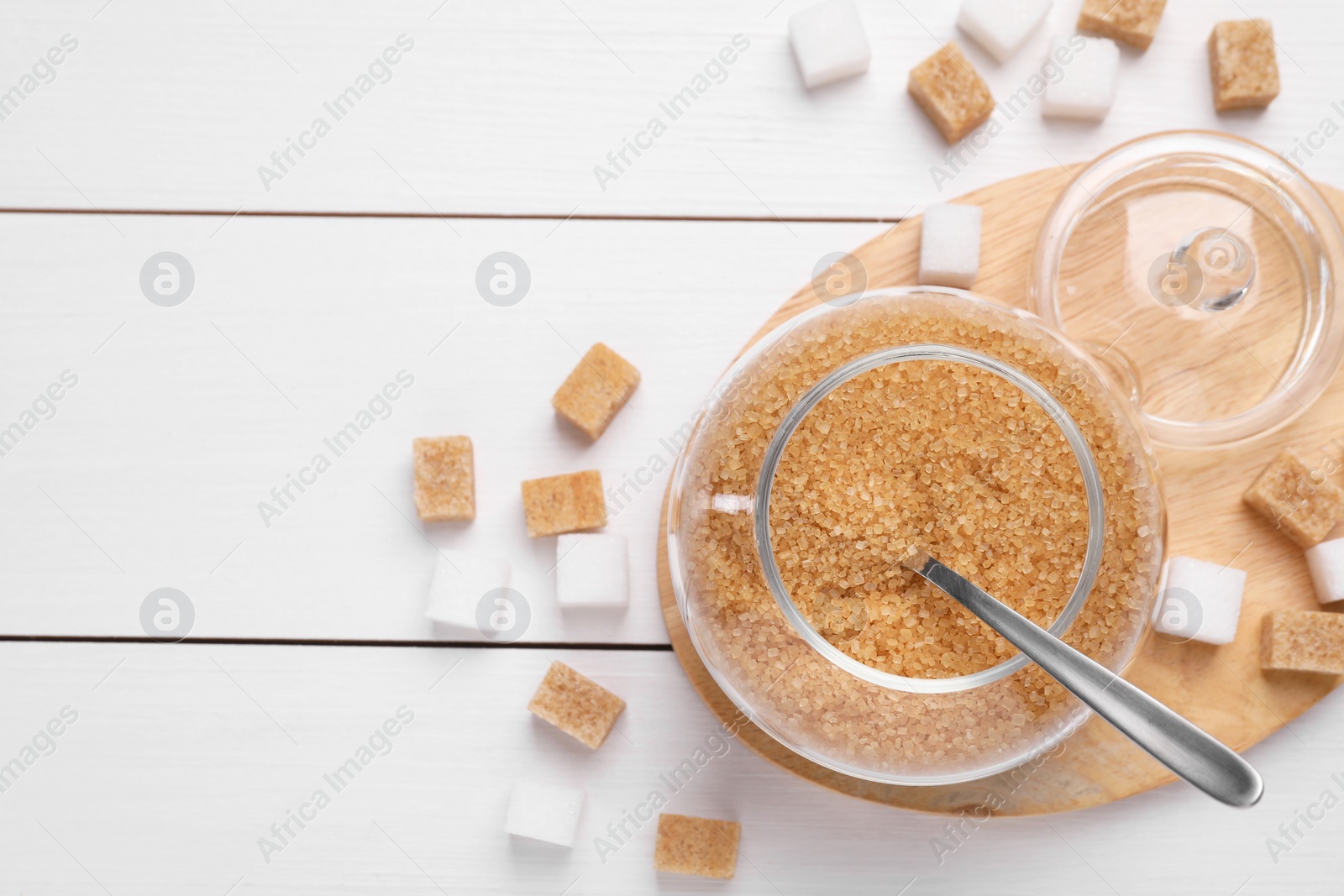 Photo of Jar and spoon with brown sugar on white wooden table, flat lay. Space for text