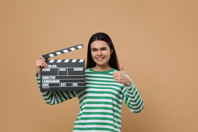Photo of Happy actress with clapperboard showing thumbs up on beige background. Film industry