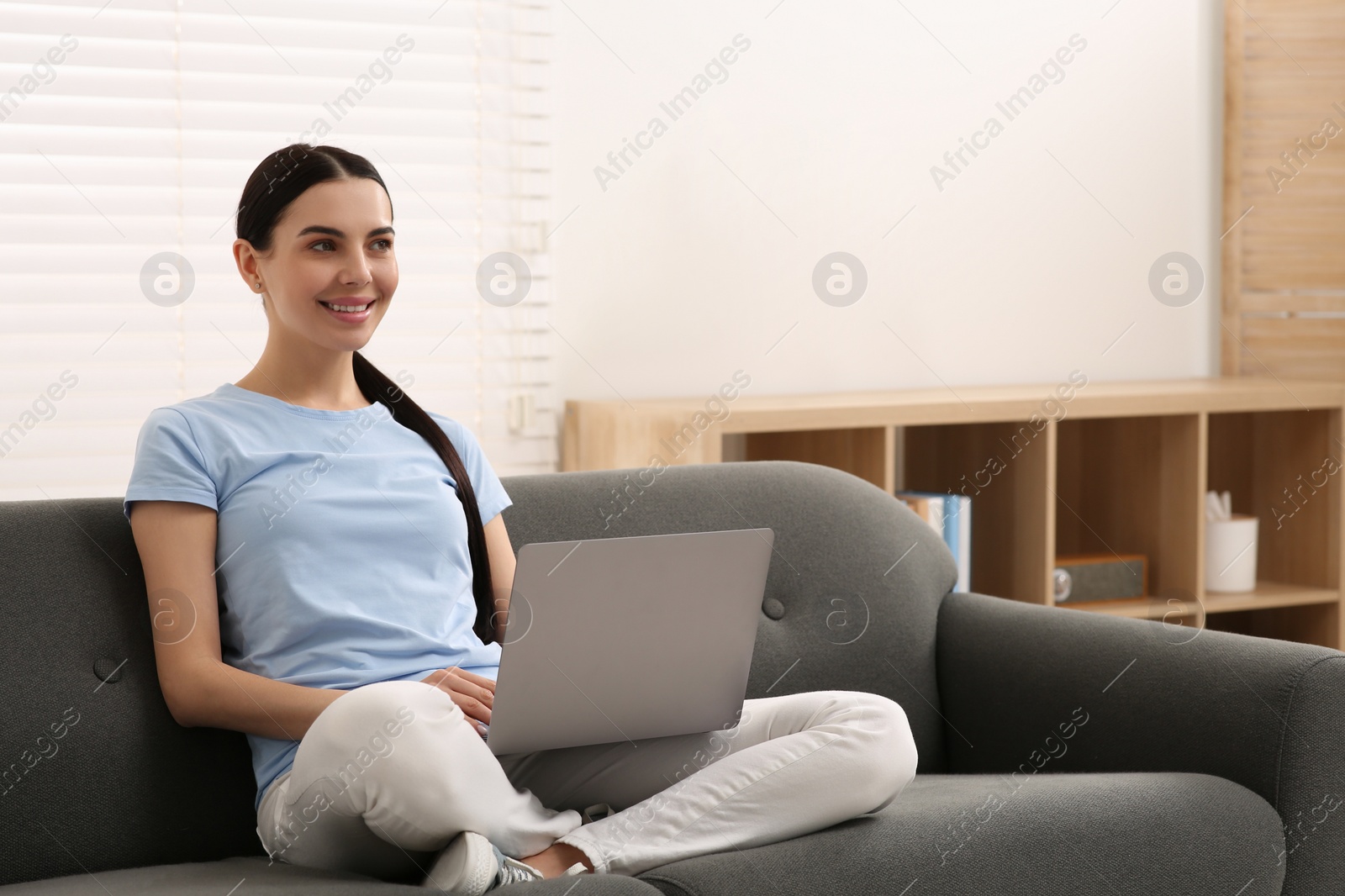 Photo of Happy woman working with laptop on sofa at home